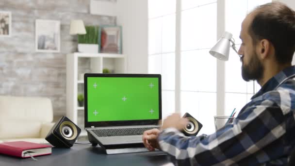 Над збільшенням плеча в кадрі людини, дивлячись на ноутбук з зеленим екраном — стокове відео