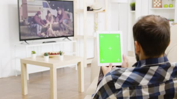 Homem olhando para um filme na TV enquanto segurando uma tela verde tablet digital PC — Vídeo de Stock