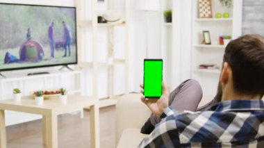 Beyaz adam elinde dikey olarak yeşil bir ekran telefonu tutuyor.
