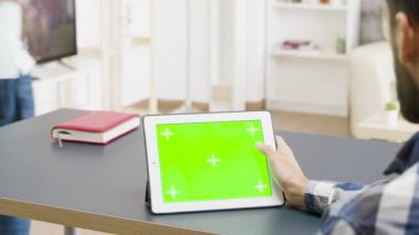 Güzel ve aydınlık dairede yeşil ekran dijital tablet üzerinde çalışan erkek.
