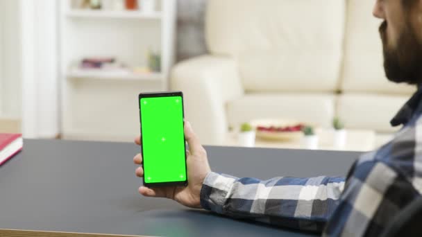Mann hält ein Telefon mit grünem Bildschirm in modernem und hellem Wohnraum — Stockvideo