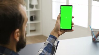 Yeşil ekranlı telefona bakan adam.