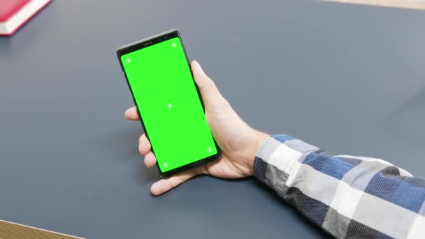 Άντρας κρατώντας ένα πράσινο τηλέφωνο οθόνη στο τραπέζι — Αρχείο Βίντεο