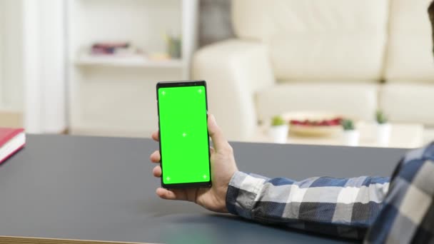 テーブルの上に緑の画面の電話を保持している男のパララックスショットでズーム — ストック動画