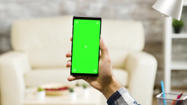 Segurando verticalmente um telefone tela verde na sala de estar — Vídeo de Stock