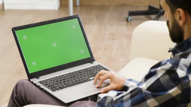 Hombre en el sofá mirando a la computadora portátil de pantalla verde — Vídeos de Stock