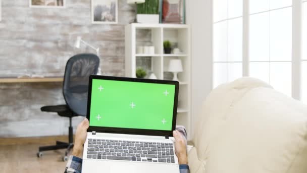 Man lying on the sofa and holding a green screen laptop — Stock Video