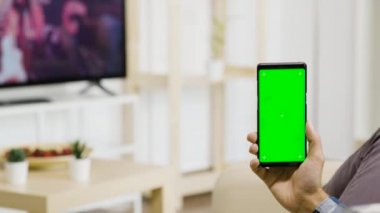 Modern ve iyi aydınlatılmış oturma odasında dikey olarak yeşil ekranlı bir telefon tutuyordu.