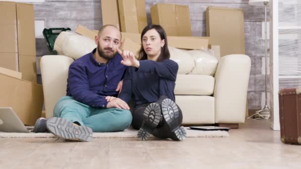 Pareja joven sentada en el suelo de su nuevo apartamento — Vídeos de Stock