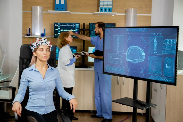 Paciente que tiene un escáner cerebral y su actividad se ve en la pantalla grande mientras los médicos hablan en la parte posterior —  Fotos de Stock