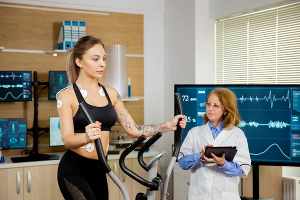 Athlète féminine qui effectue des tests sur le stepper et a des électrodes sur elle et le médecin la suit — Photo