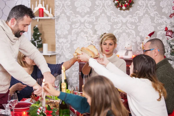 Homem adulto cortando carne enquanto os membros da família estão passando o pão um para o outro na véspera de Natal — Fotografia de Stock