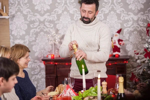 Homem adulto na véspera de Natal sorrindo e abrindo uma garrafa de champanhe — Fotografia de Stock