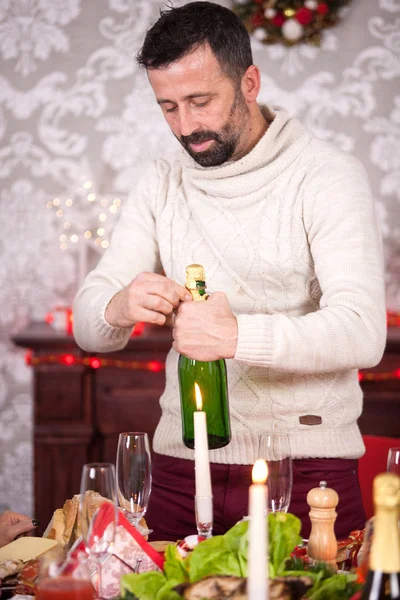 Homem adulto alegre segurando uma garrafa de champanhe celebrando o Natal com sua família — Fotografia de Stock