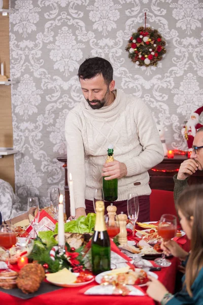 Allegro uomo adulto schiocca una bottiglia di champagne che celebra il Natale con la sua famiglia — Foto Stock