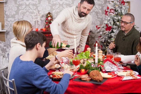 Noel ziyafetinde aile birbiriyle konuşuyor ve üyelerden biri herkese şampanya dolduruyor. — Stok fotoğraf