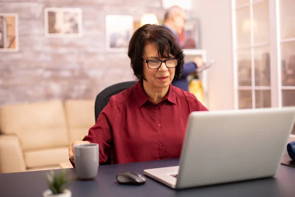 Vecchia donna nei suoi anni '60 utilizzando un computer portatile moderno nella sua casa accogliente — Foto Stock