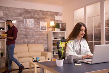 Güzel beyaz kız arkadaş oturma odasında dizüstü bilgisayarla çalışıyor.