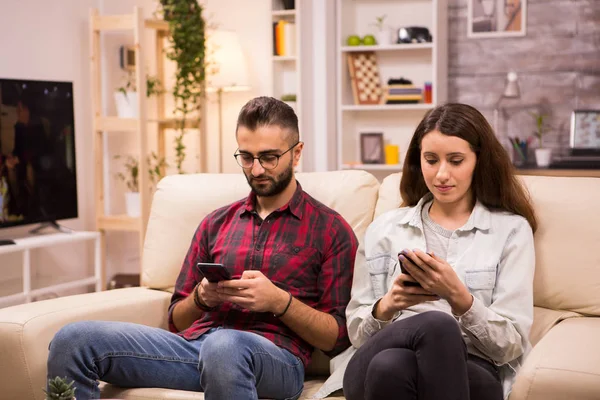 Парень и девушка пользуются своими телефонами, сидя вместе на диване — стоковое фото