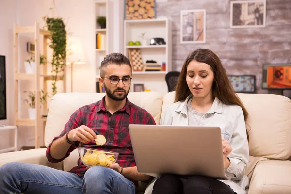 Přítel jíst chipsy, zatímco jeho přítelkyně je prohlížení na notebooku — Stock fotografie