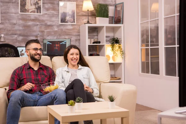 Jovem casal alegre sentado no sofá e assistindo a um filme na TV — Fotografia de Stock