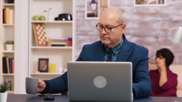 Oude man genieten van een kopje koffie tijdens het werken op laptop — Stockvideo