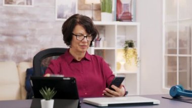 Tablet ve telefon kullanan gözlüklü yaşlı kadın.