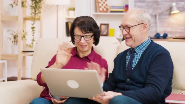 Äldre par som sitter på soffan och håller laptop under ett videosamtal. — Stockvideo