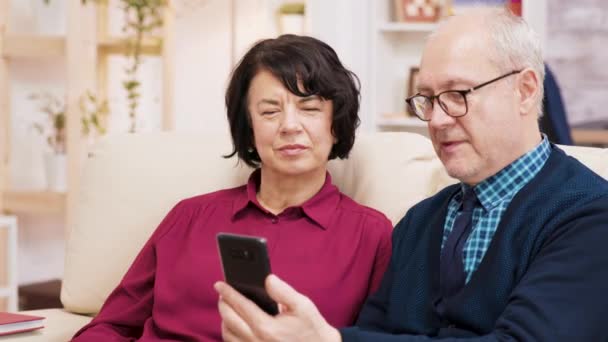 Boldog idősek, akik videóhívást tartanak a kanapén a nappalijukban. — Stock videók
