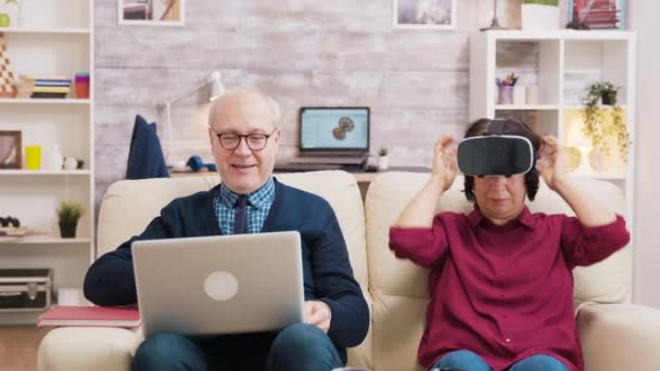 Пожилая женщина сидит на диване в очках виртуальной реальности — стоковое видео