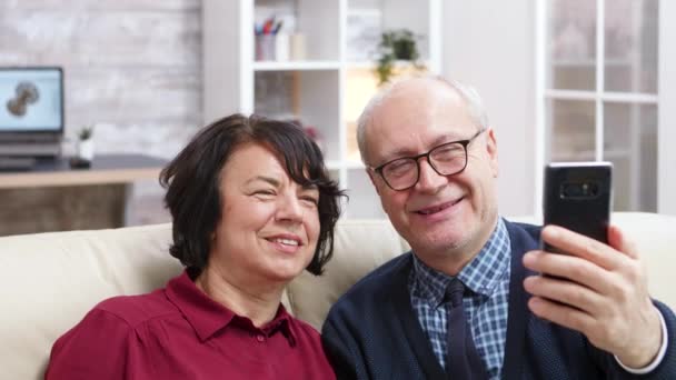 Glada gamla par sitter på soffan och tar en selfie — Stockvideo