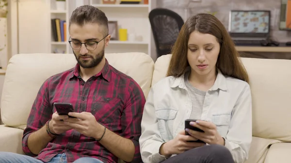 Casal distante sentado no sofá usando seus telefones — Fotografia de Stock