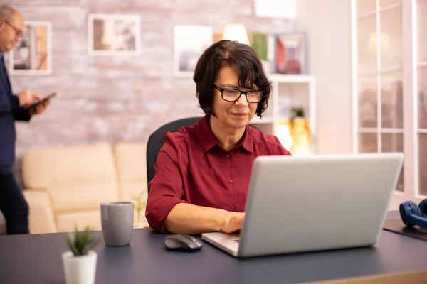 Vecchia donna nei suoi anni '60 utilizzando un computer portatile moderno nella sua casa accogliente — Foto Stock