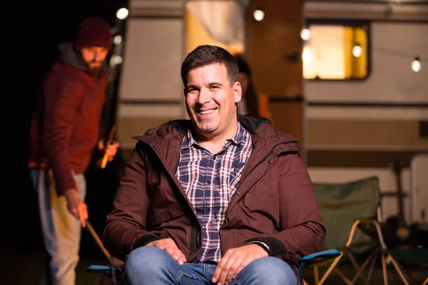 Retrato del joven sonriendo y sentado en el chiar de camping —  Fotos de Stock