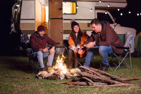 Grupo de amigos que se relajan y ríen juntos alrededor del fuego del campamento — Foto de Stock