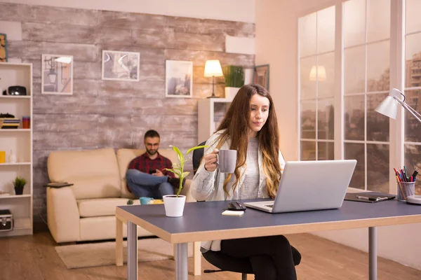 Mulher bonita segurando uma xícara de café enquanto olha para o laptop — Fotografia de Stock