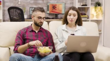 Dizüstü bilgisayarda gezinirken soda içip cips yiyen çift.