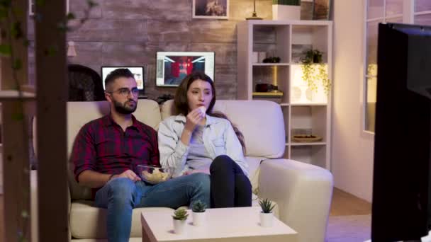 Ζευγάρι κάθεται στον καναπέ και τρώει πατατάκια ενώ βλέπει μια ταινία — Αρχείο Βίντεο