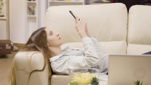 Hübsches Mädchen entspannt sich auf der Couch mit ihrem Smartphone — Stockvideo