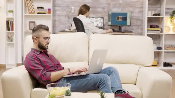 Fešák na volné noze pracuje na notebooku, zatímco sedí na gauči — Stock video