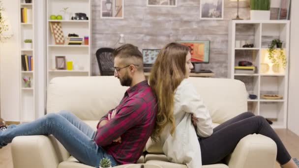 Couple sitting back to back on the couch with arms crossed — Stockvideo