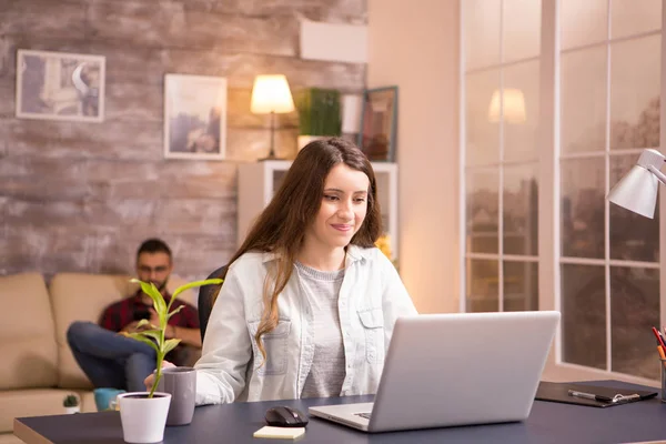 Молода жінка посміхається під час роботи на ноутбуці і тримає чашку кави — стокове фото