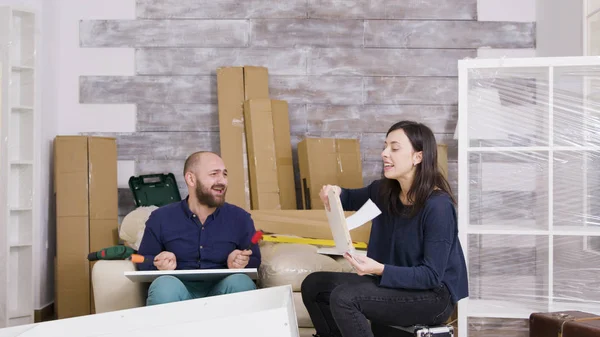Молодая пара смеется, собирая мебель в своей квартире — стоковое фото