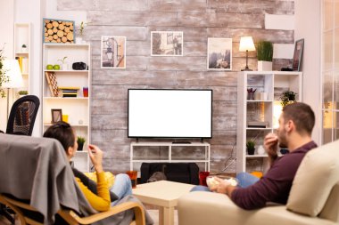 Oturma odasındaki izole edilmiş televizyon ekranına bakan çift.