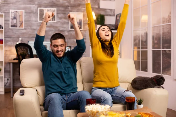Casal feliz torcendo por sua equipe favorita enquanto assiste TV na sala de estar — Fotografia de Stock