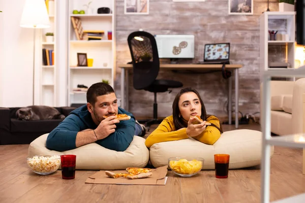 Pár sedí na podlaze a dívají se na televizi v obýváku — Stock fotografie