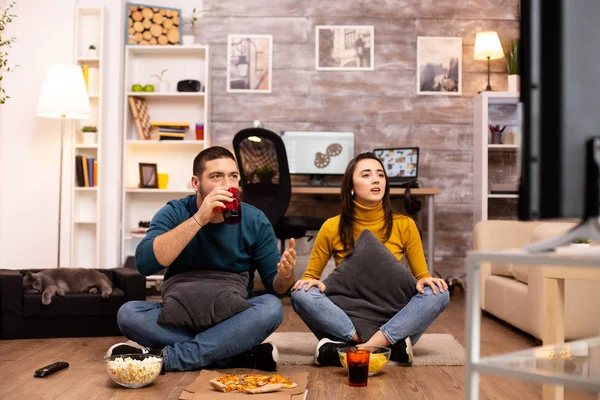 Pár sedí na podlaze a dívají se na televizi v obýváku — Stock fotografie