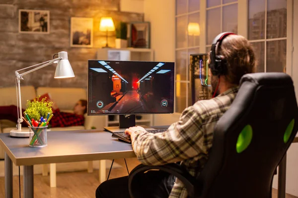 ライブルームで夜遅くに彼の強力なPCコンピュータ上でシューティングゲームをプレイゲーマー男性のバックビュー — ストック写真