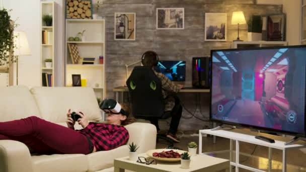 Женщина лежит на диване и играет в видеоигры с помощью наушников vr — стоковое видео