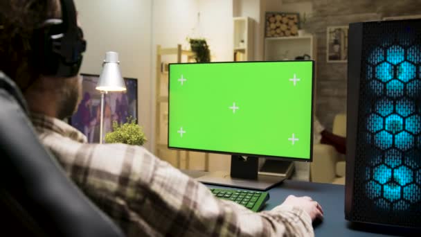 Kulaklıklı adam yeşil ekranlı bilgisayarda oyun oynuyor. — Stok video